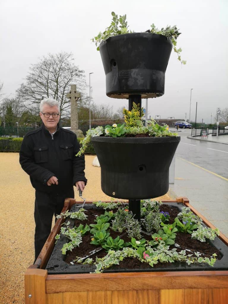 Town Mayor standing by wooden planters with green plants