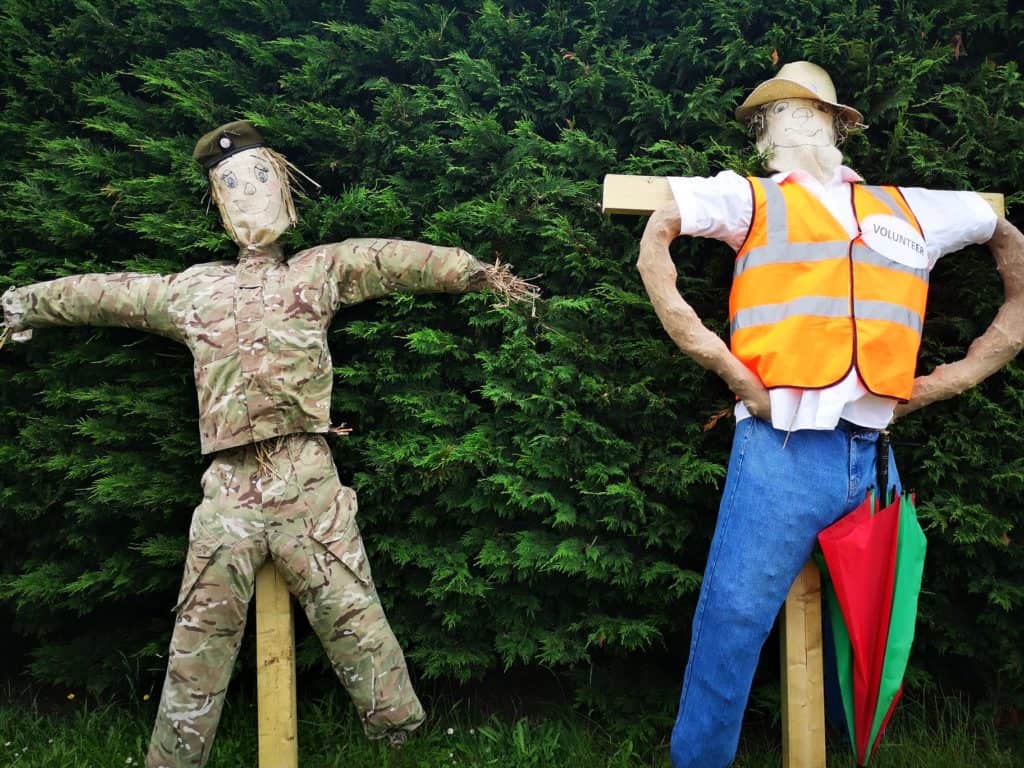 two scarecrows, one dressed like a solider and one dressed in orange high vis as a volunteer