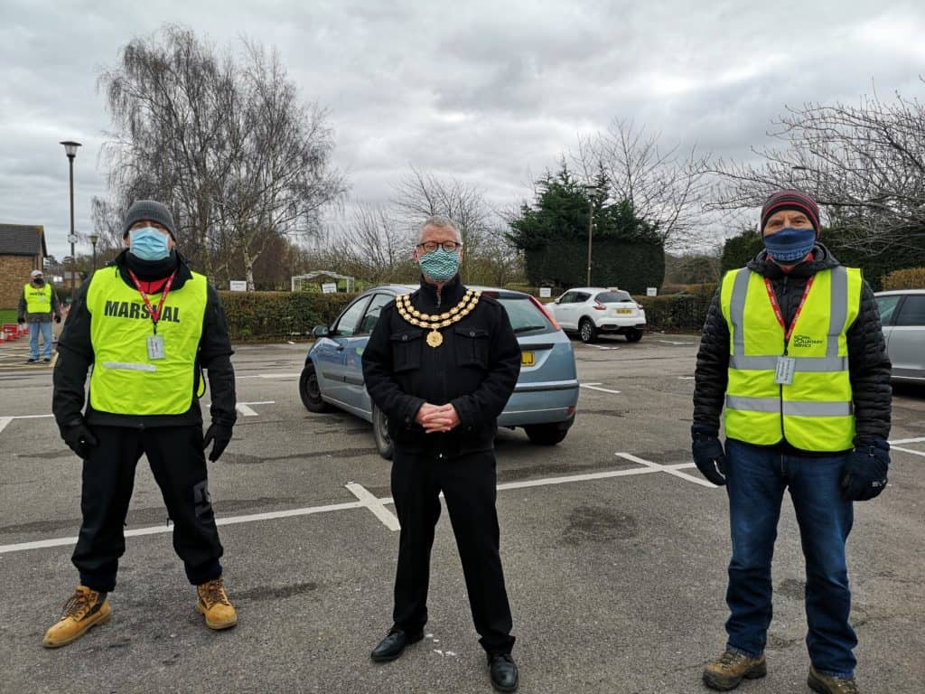 Town mayor wearing mayoral chain and three male volunteers in yellow high vis jackets standing in car park of The Rufus Centre