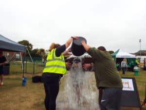 Two people pouring bucket of water over person